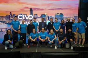 A group of people, including Civo staff members, pose together on stage in front of a large screen displaying a cityscape with the Civo logo prominently displayed. 